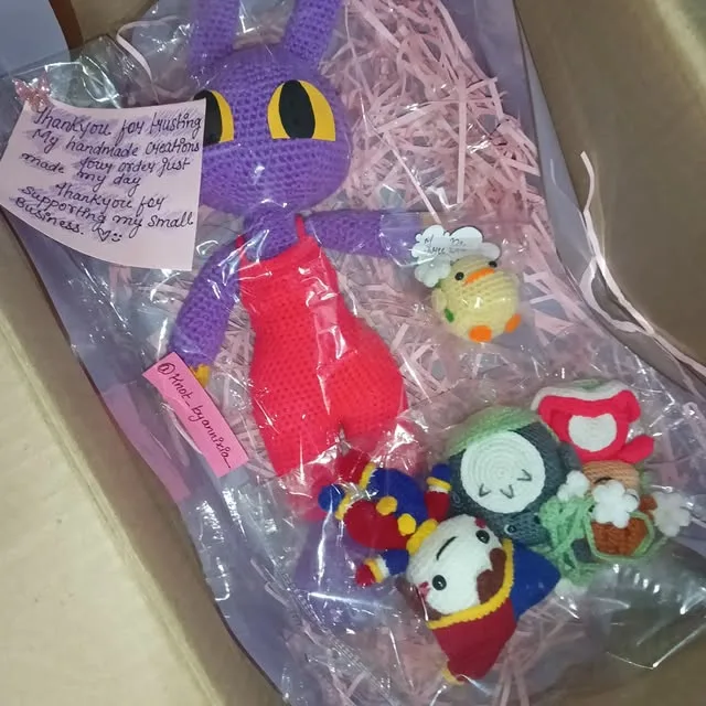 An open parcel of crochet goodies: a purple character plush, keychains and a handwritten note