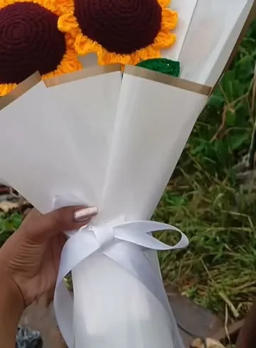 Two crochet sunflowers in a cream wrap held up outdoors
